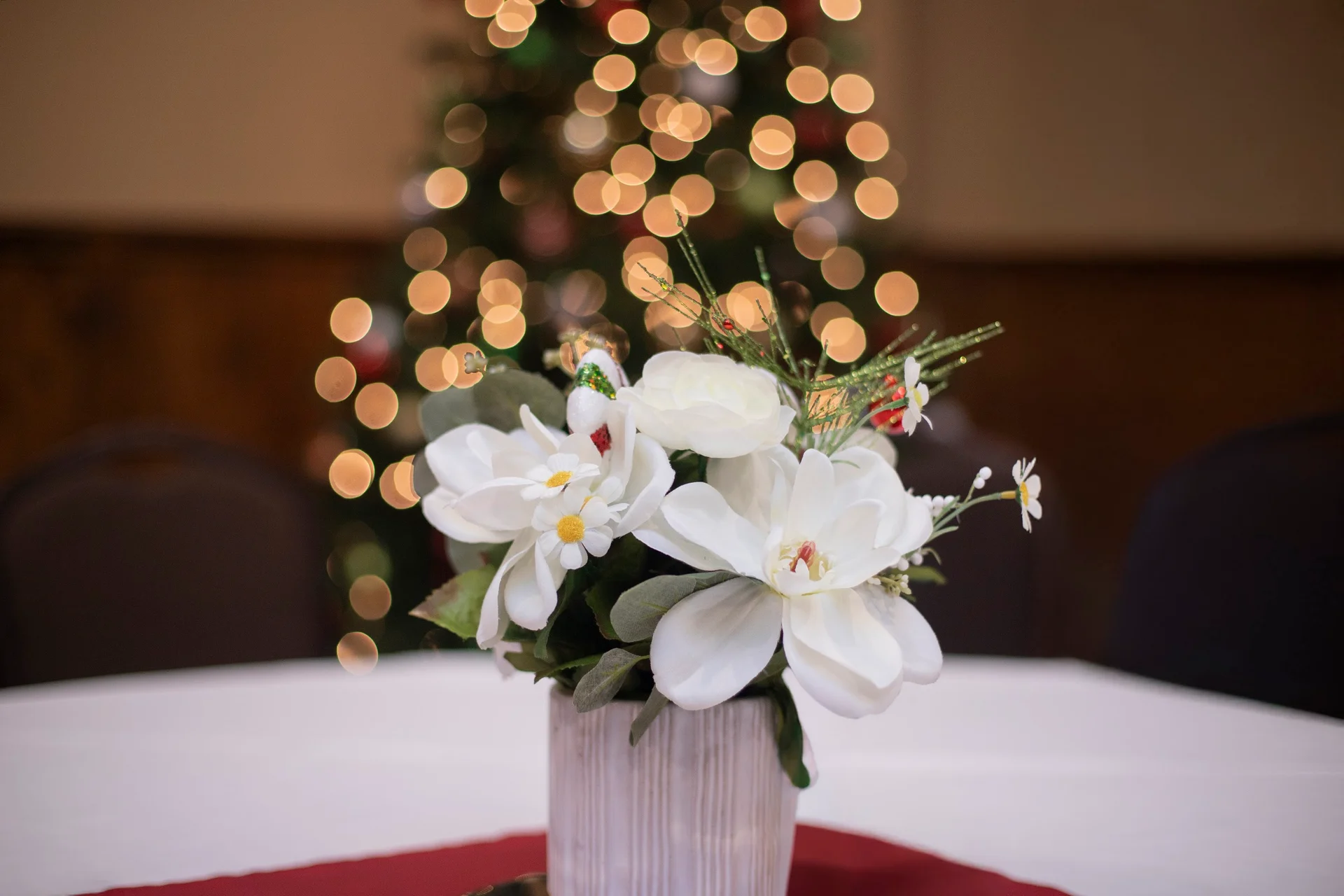 White flowers on a table with Christmas tree lights behind them