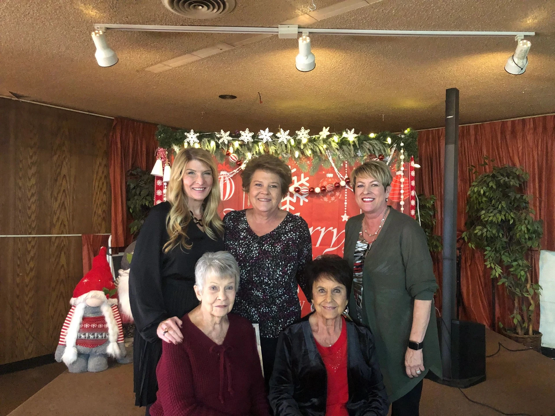 Five women smiling in front of a festive Christmas backdrop