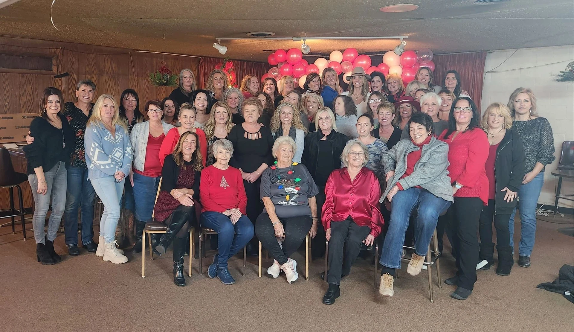 Mamma Bears gathered in rows, smiling beneath red and white balloons at a past community gathering